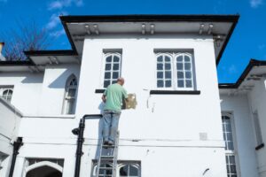 Man on ladder painting exterior of a house